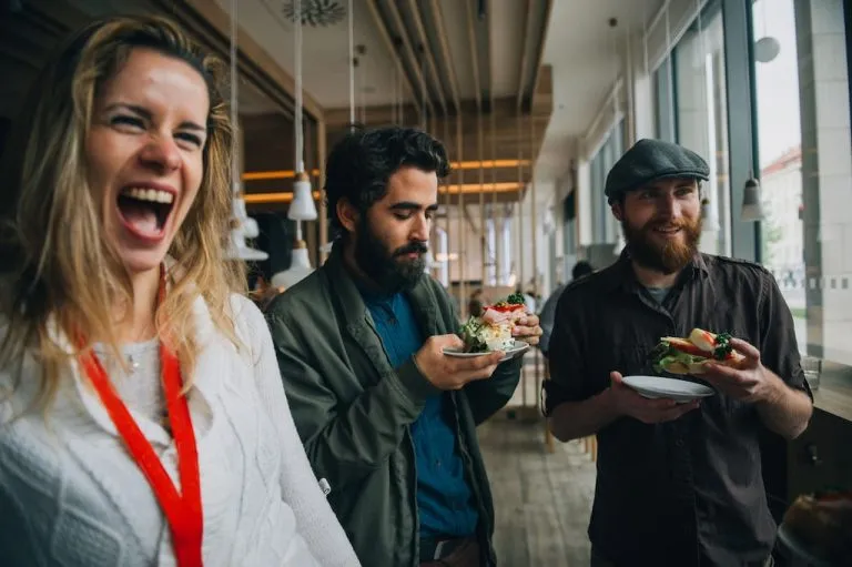 three guests on a food tour in Prague: two men eating open-faced sandwiches and a women on the side laughing at something outside of the image frame