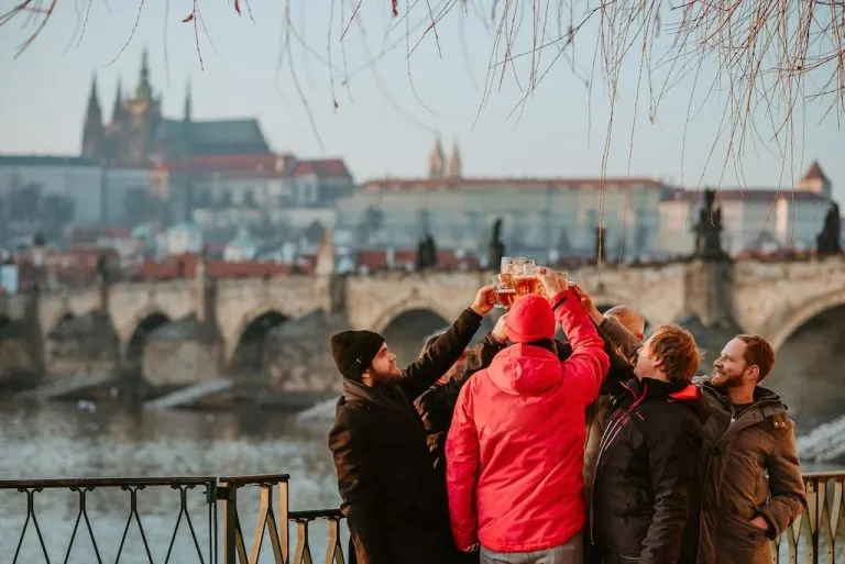 a group of travelers and their tour guide standing by the Vltava River with beer glasses raised to a toast