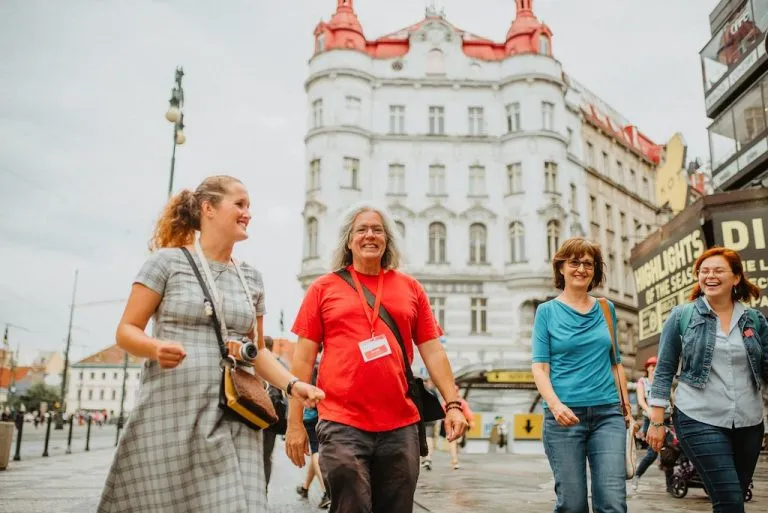 a Prague City Adventures tour guide in a red shirt leading a group of female tourists through the streets of Prague's city center