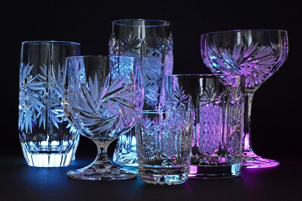 6 different glasses with intricate patterns made of high-quality Bohemian crystal, standing on a black background with a purple-bluish light