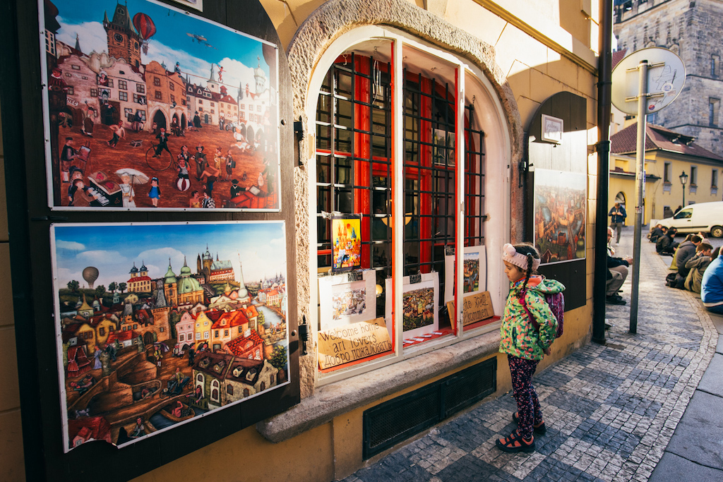 a little girl looking at paintings of Prague in the window of the Gallery by Jiri Stastny