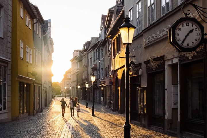 a narrow street in Prague's Little Quarter with a clock on the side of a building