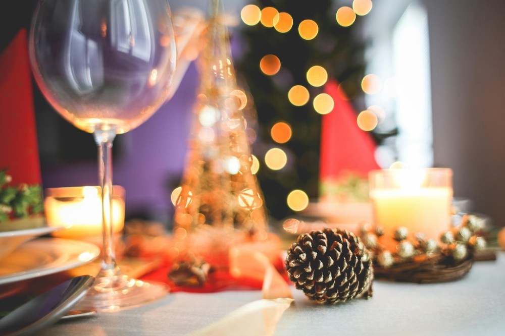 an empty wine glass on a table with a pinecone and other Christmas decorations, with a Christmas tree in the background