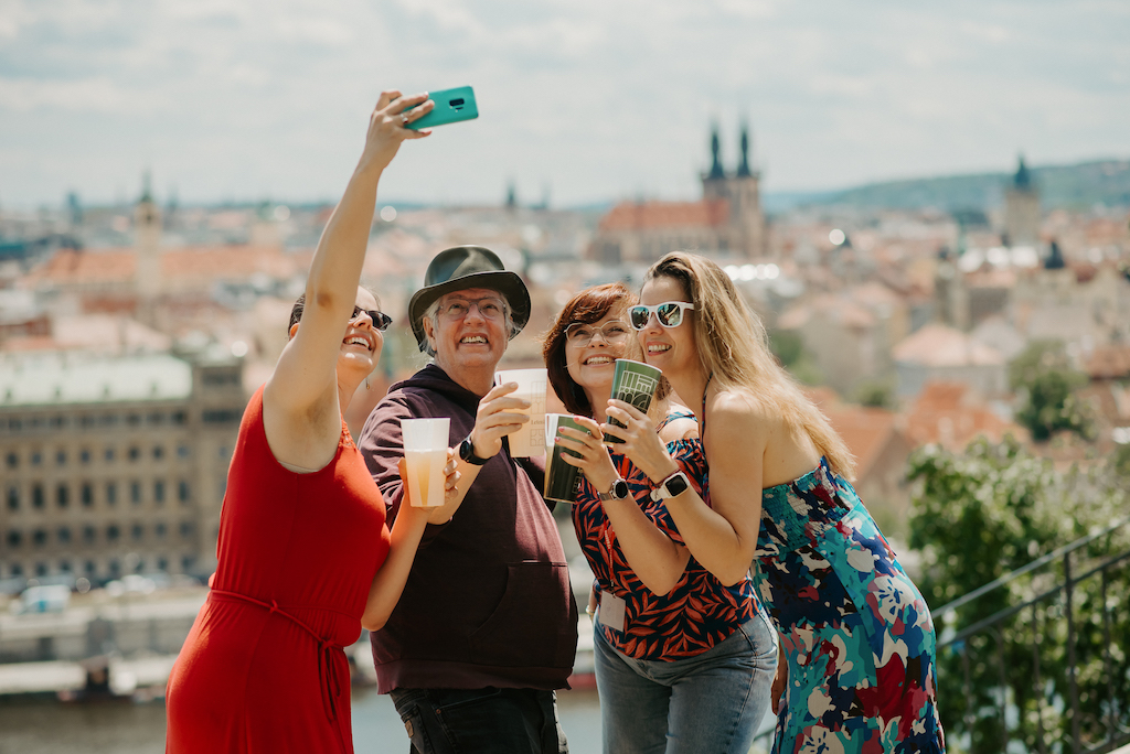 a group of tourists taking a selfie with a panoramic view of Prague in the background